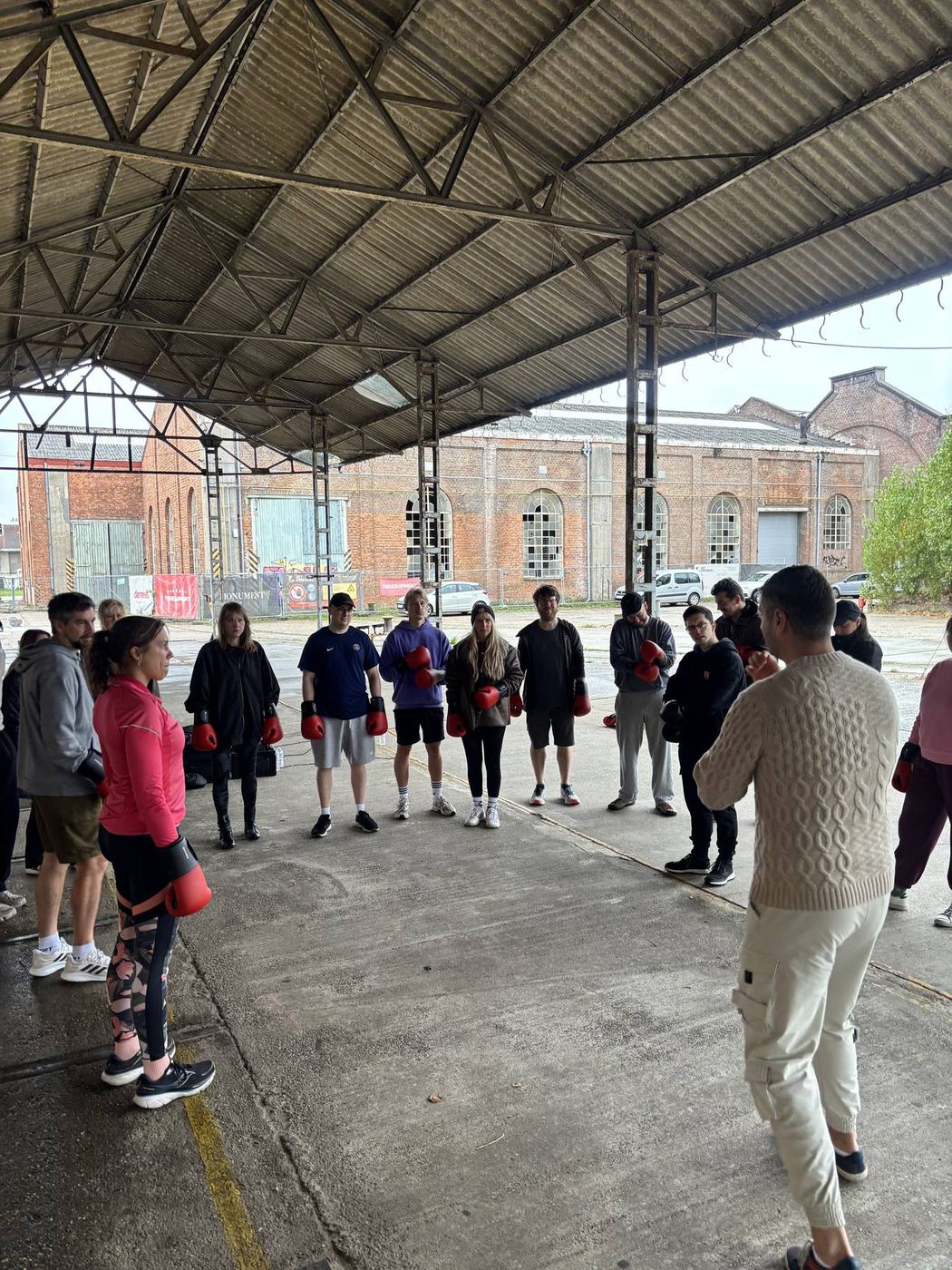 Coach legt de oefening uit aan de groep in een kring onder het afdak in Gentbrugge